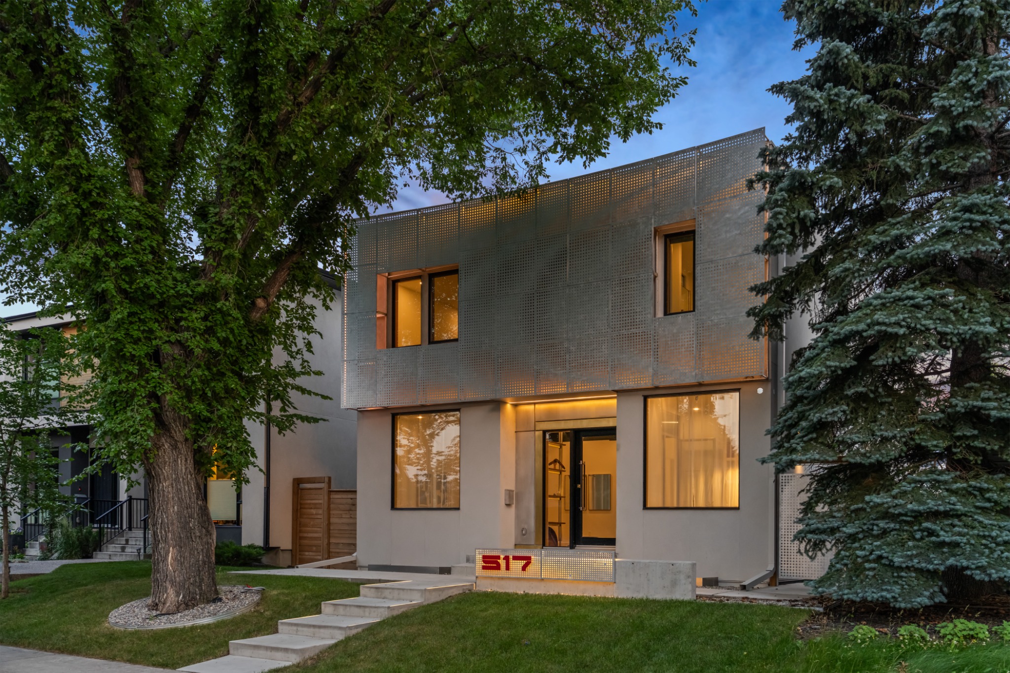 Chinookwinds House at dusk, framed by mature trees and warm interior lighting